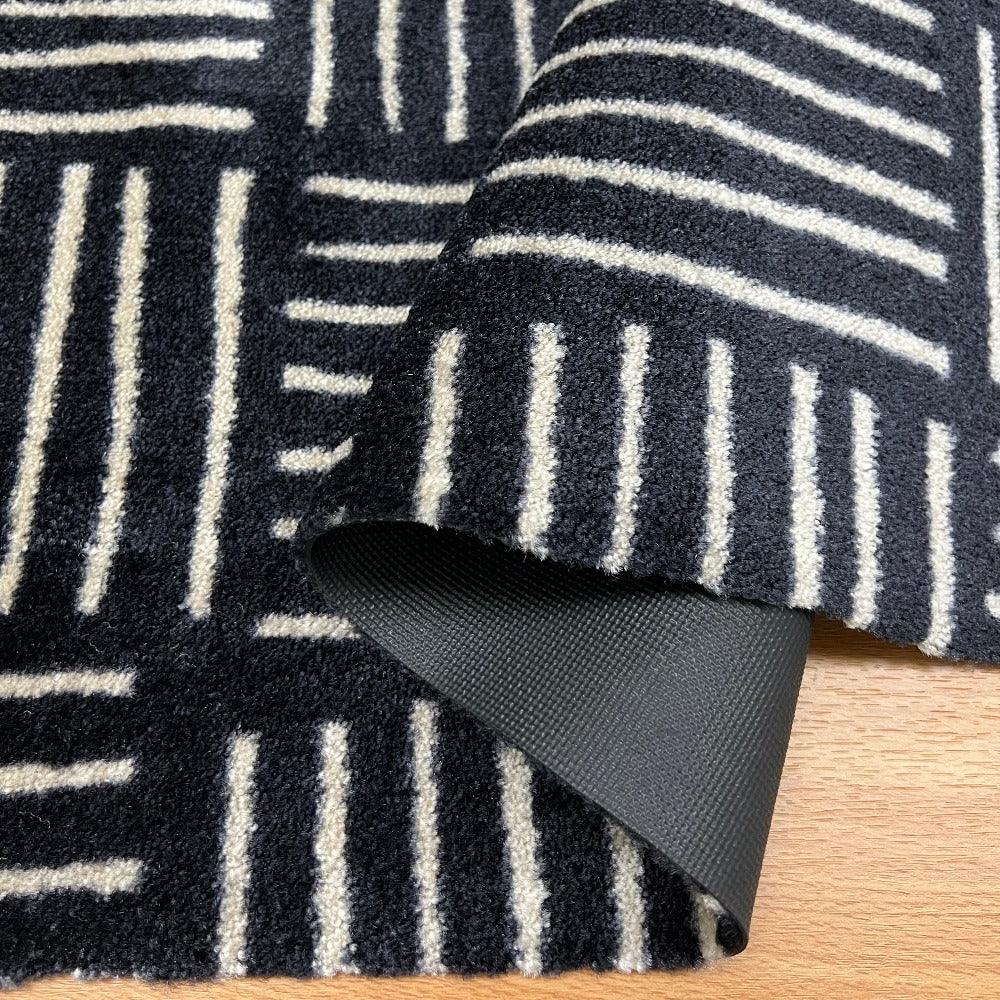 Black and white patterned rug with a corner folded over, showing a textured surface.