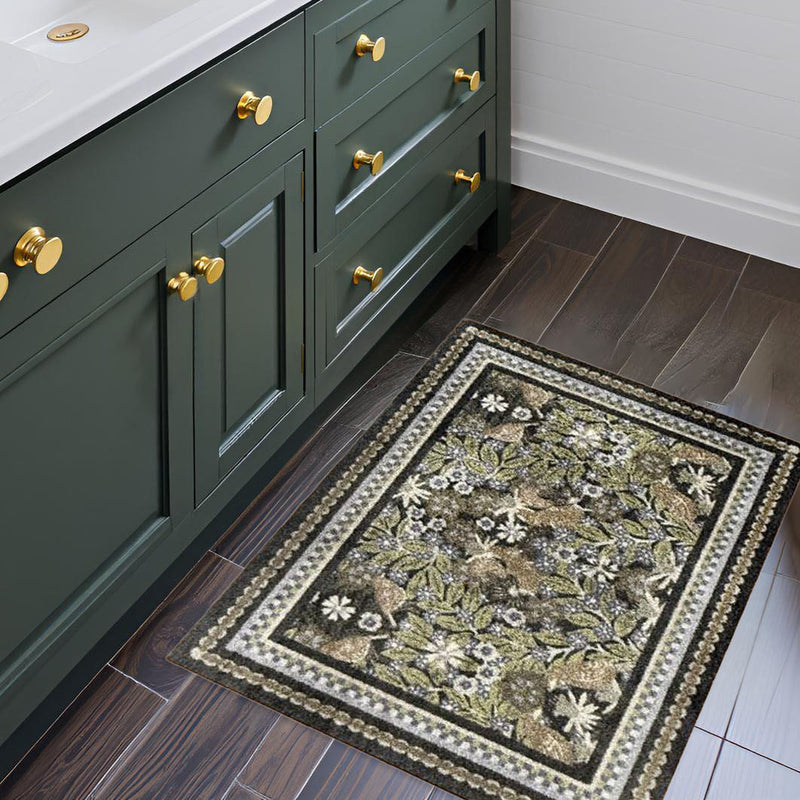 Bathroom with green vanity, gold fixtures, and a decorative rug on wooden flooring.
