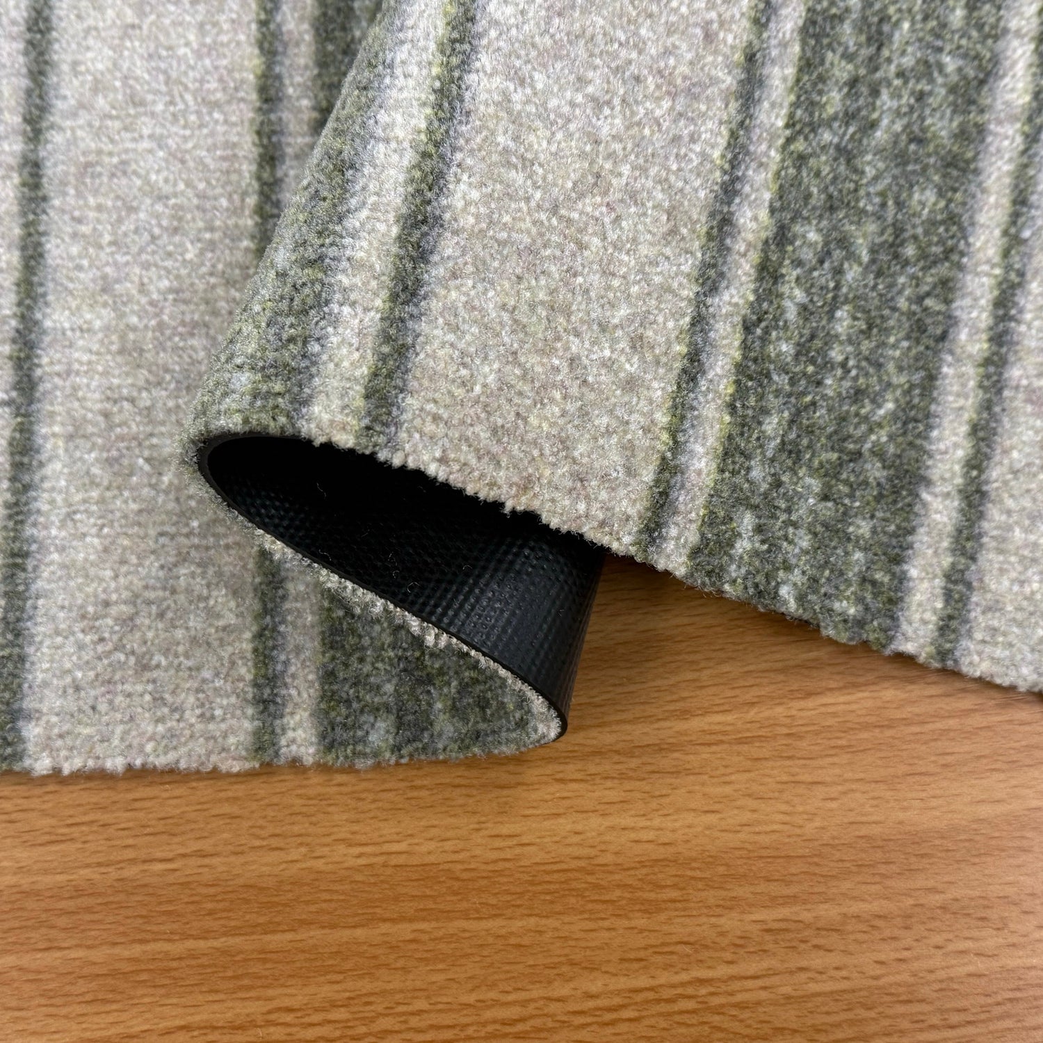 Close-up of a textured Green and White rug corner on a wooden floor.