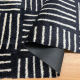 Black and white patterned rug with a corner folded over, showing a textured surface.