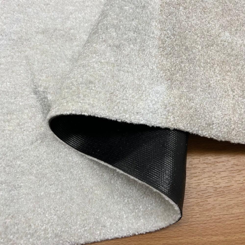Close-up of a textured gray carpet roll with a visible backing on a wooden floor.
